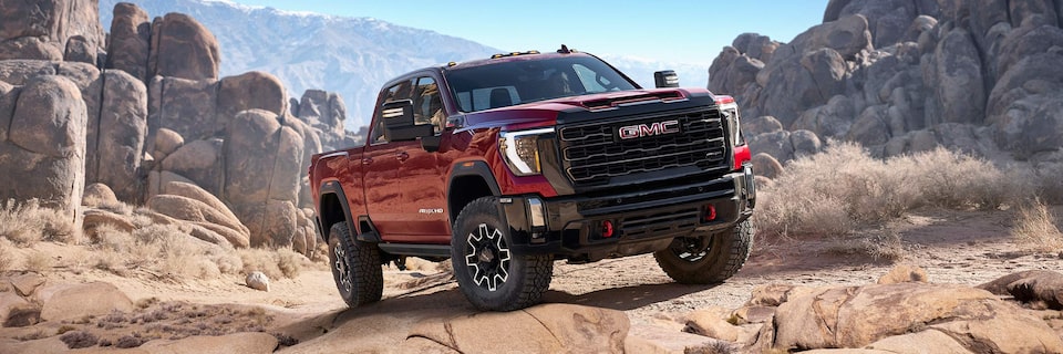 Front Three-Quarter View of a Red GMC Sierra HD AT4X AEV Parked on Rough Terrain