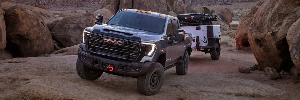 Front Three-Quarter View of the GMC Sierra HD AT4X AEV Driving Off-Road While Pulling a Trailer