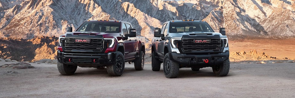 The 2024 GMC Sierra HD AT4X and AT4X AEV Edition Pickup Trucks Parked Next to Each Other with a Mountain View in the Distance