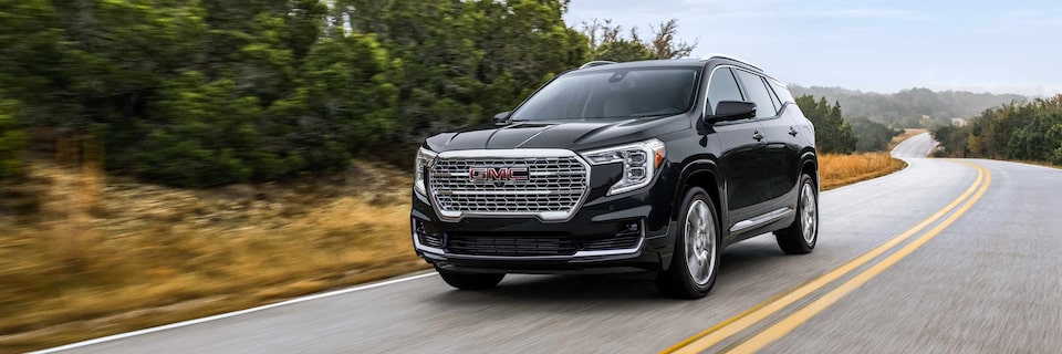 Wide View of a GMC SUV Driving on an Open Road Lined by Trees