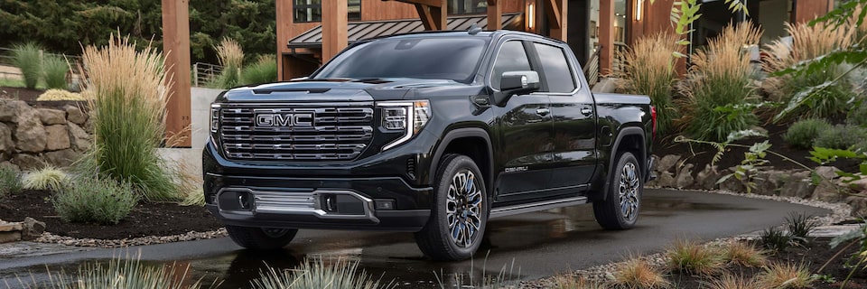 Front Three-Quarters View of a GMC Denali Truck Surrounded by Lanscaping in Front of a House