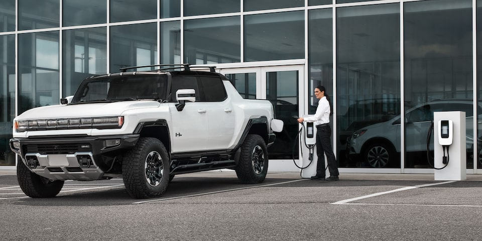 GMC Hummer EV Truck Sitting in Front of a Dealership Being Plugged Into Charging Station