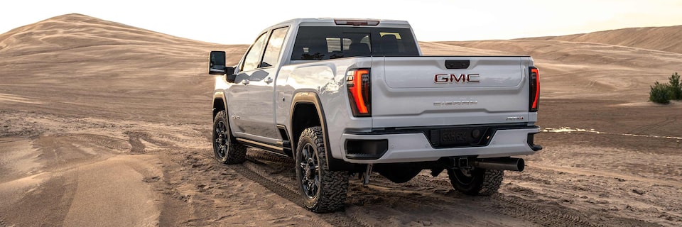 Rear Three-Quarter View of a GMC Sierra HD AT4 Truck on a Sandy Path at Sunset