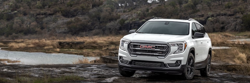 A GMC Terrain AT4 SUV Driving Through the Mud With Trees in the Background