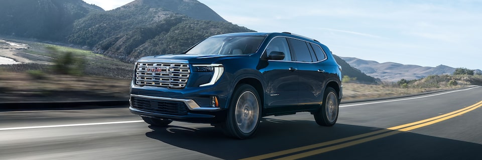 Wide Front Three-Quarters View of a GMC Acadia SUV Driving on an Open Road with Mountains in the Background