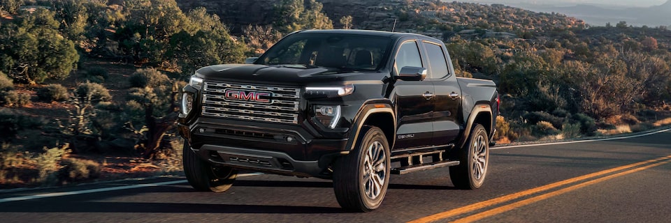 Front Three-Quarters View of a GMC Canyon Denali Truck Driving on an Open Road at Sunset