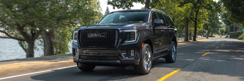 Close-up Front Three-Quarters View of a GMC Yukon Denali Ultimate Driving on a Tree-Lined Road