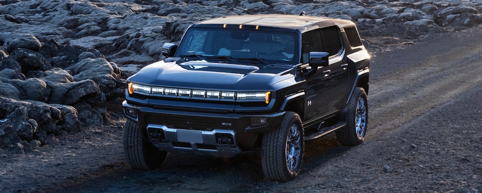 Three-Quarters View of a GMC Hummer EV SUV Going Down the Road Surrounded by Rocks