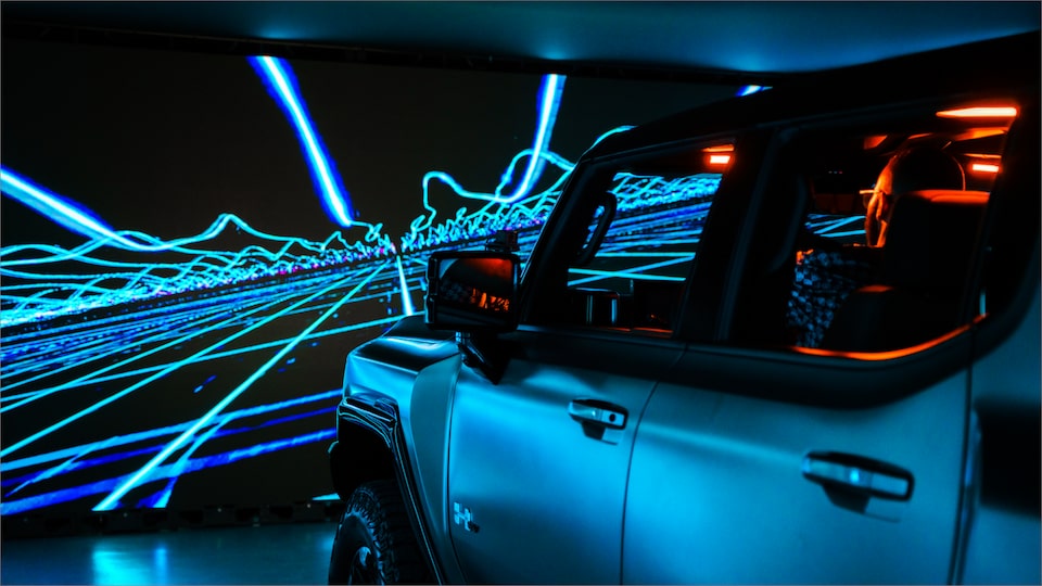 An Exterior Driver's Side Shot from the Back with Neon Lights on the Wall in Front of the GMC Hummer EV in a Showroom