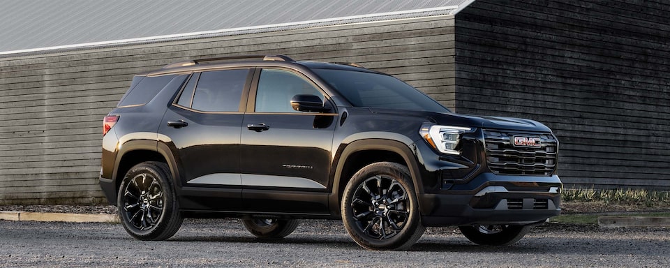 Front Three-Quarters View of a 2025 GMC Terrain Small SUV Parked Near a Wood Building