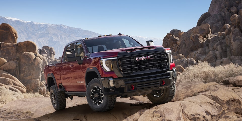 The Sierra HD AT4 Climbing an Off-Road Rocky Incline with Clear Skies & Mountains in the Distance