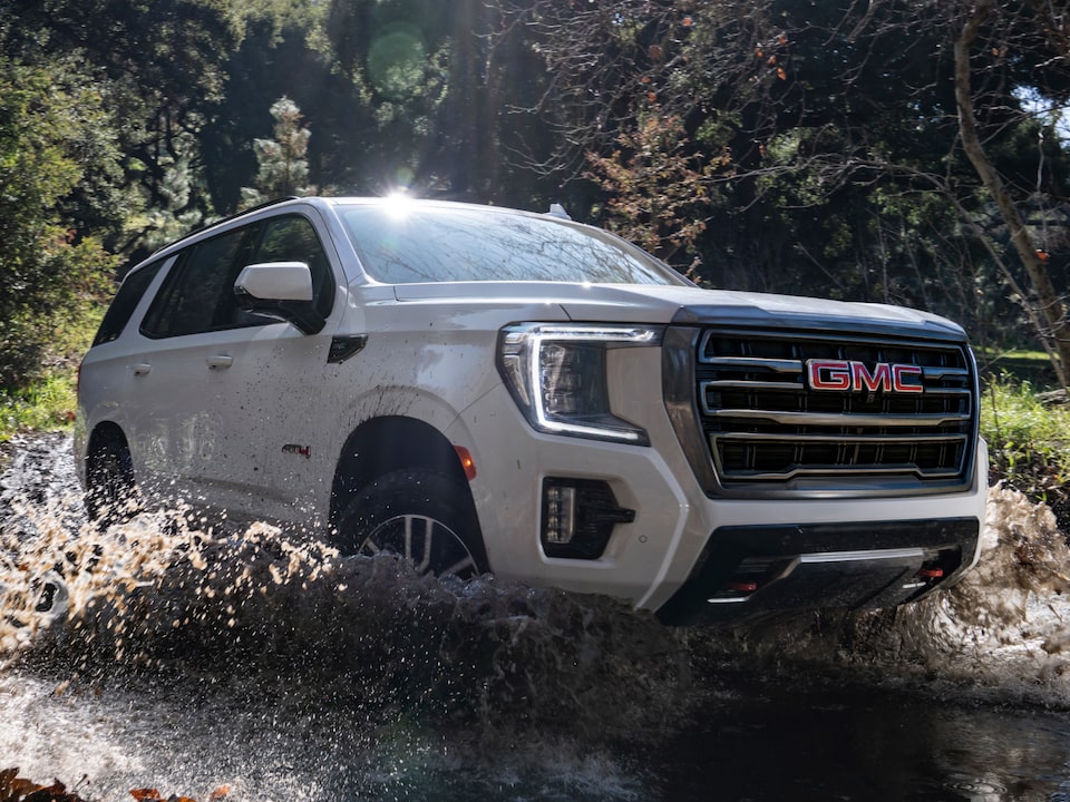 A GMC Yukon SUV Driving Though Water Surrounded by Trees