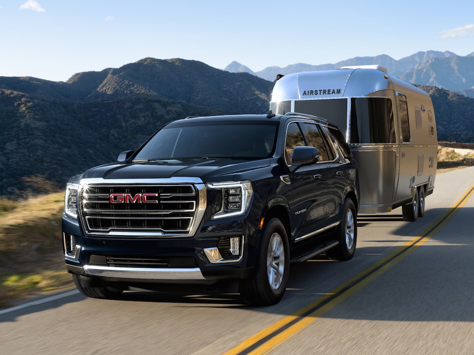 A GMC SUV Hauling a Trailer on an Open Road Lined by Mountains