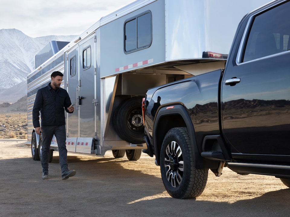 A Man Using His Smartphone and Walking to His GMC Truck with a Trailer Attached