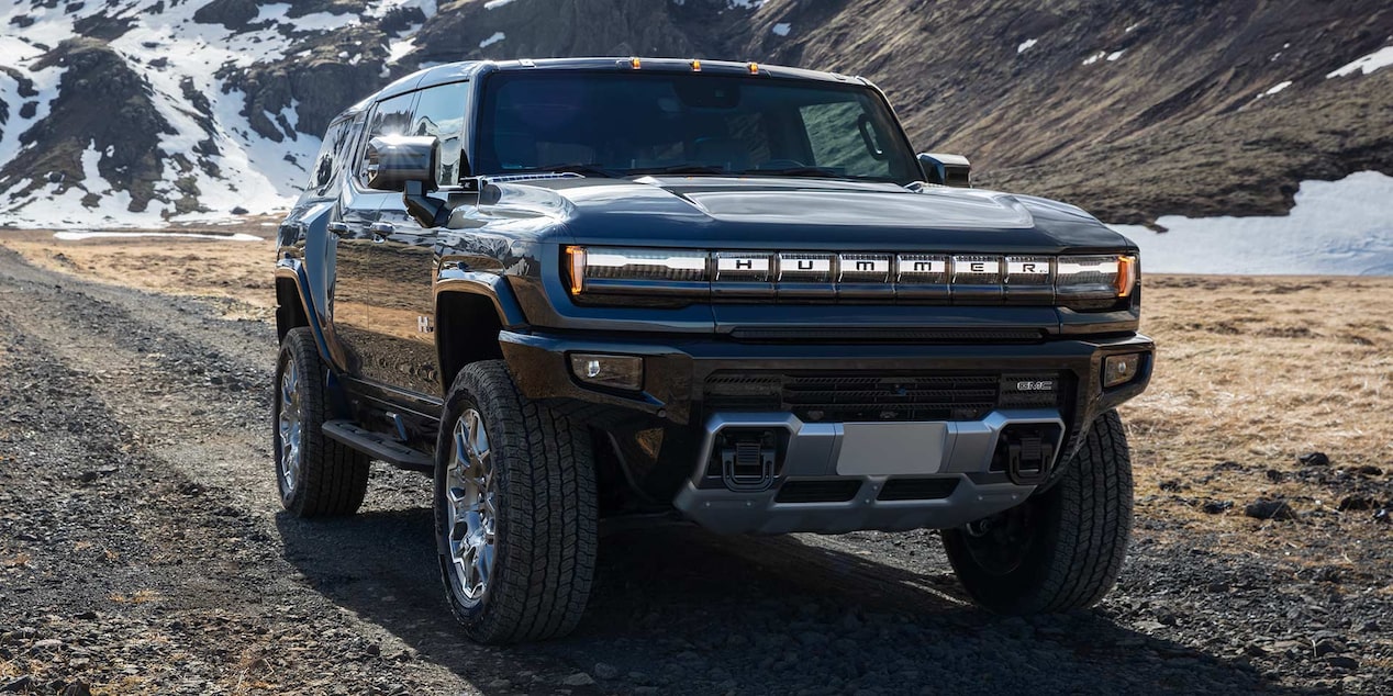 Front Three-Quarter View of the GMC HUMMER EV Pickup Truck Driving Down a Dirt Road with Mountains in the Background