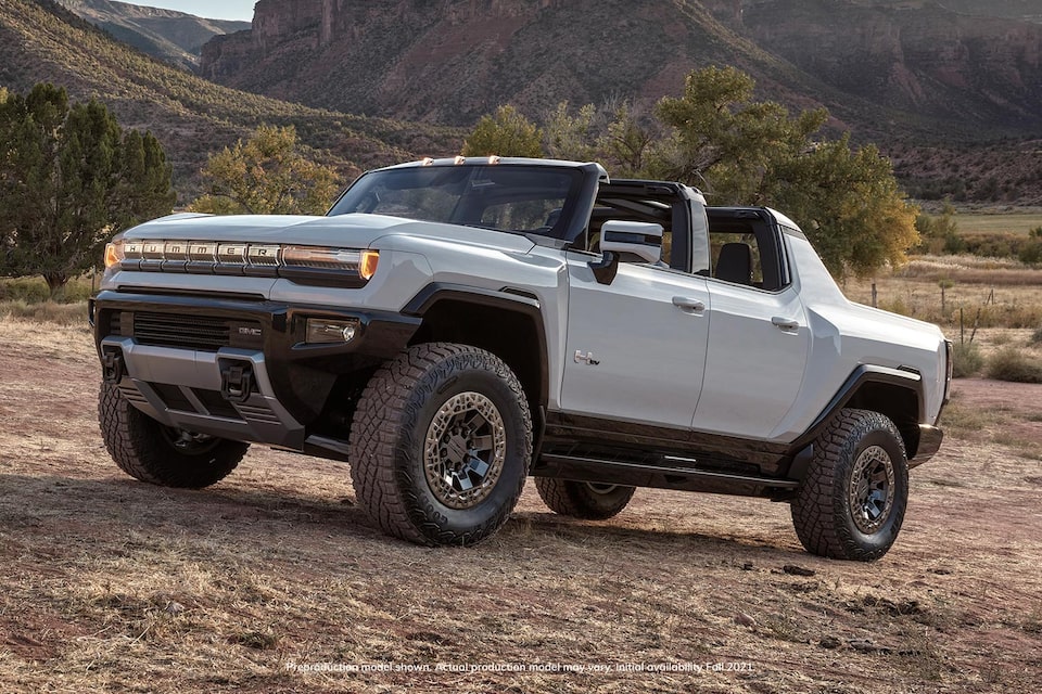 Three-Quarter Side View of a GMC HUMMER EV Pickup Truck Parked in a Valley with Luscious Green Mountains in the Background