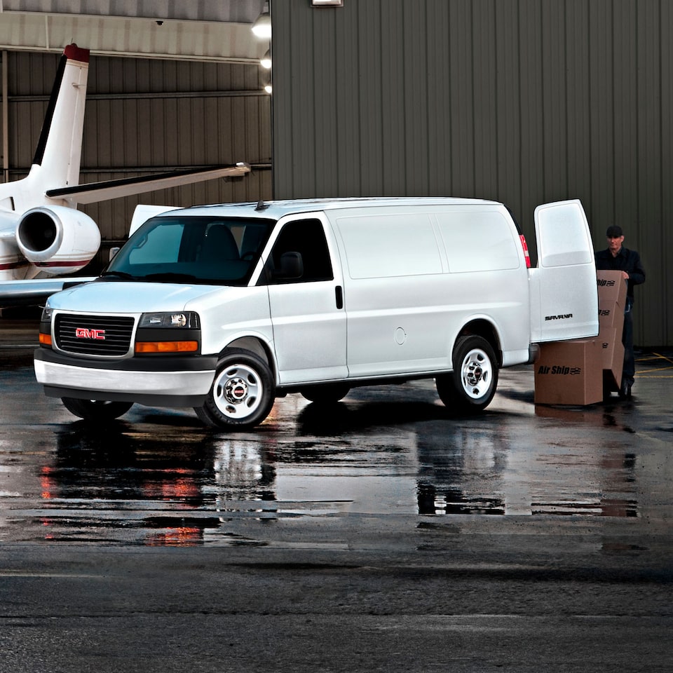 A White GMC Savana Cargo Van Parked Next to a Jet