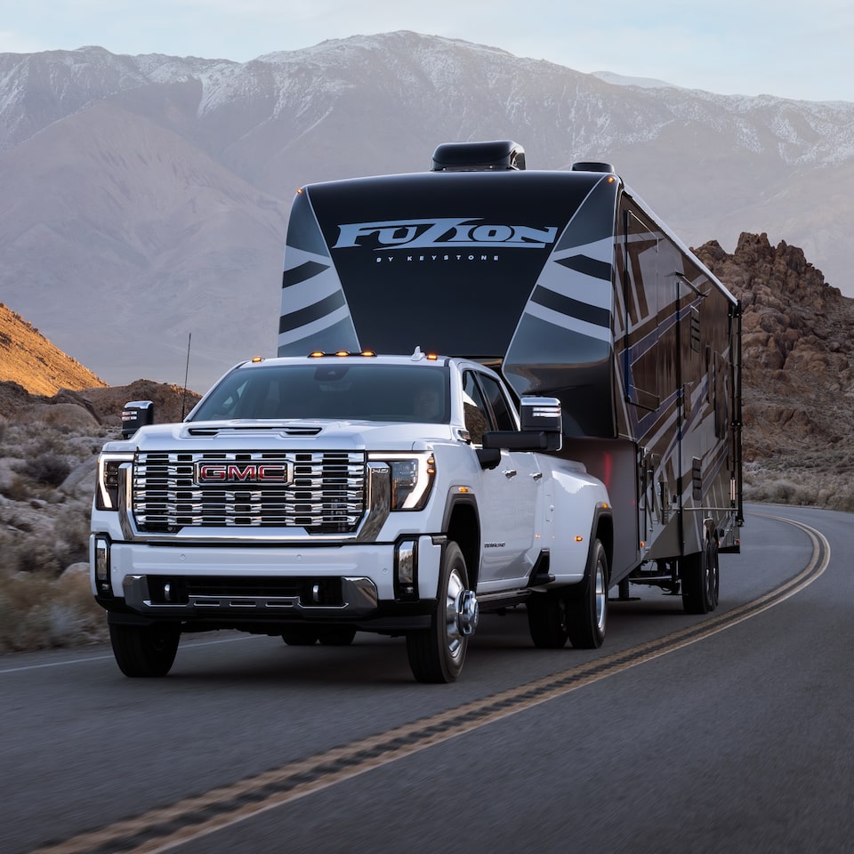 The White GMC Sierra HD Driving On-Road Towing a Trailer