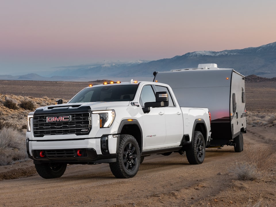 A White GMC Sierra HD Driving Off-Road Towing a Trailer