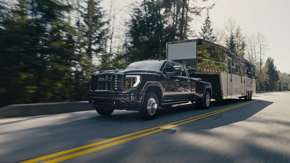 Front Three-Quarters View of a GMC Sierra HD Truck Hauling a Trailer on a Tree-Lined Road