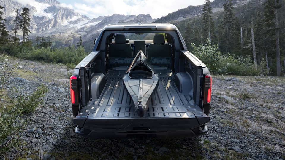 View of the Truck Bed on the GMC Sierra EV Truck Hauling a Kayak Surrounded by Mountains and Trees