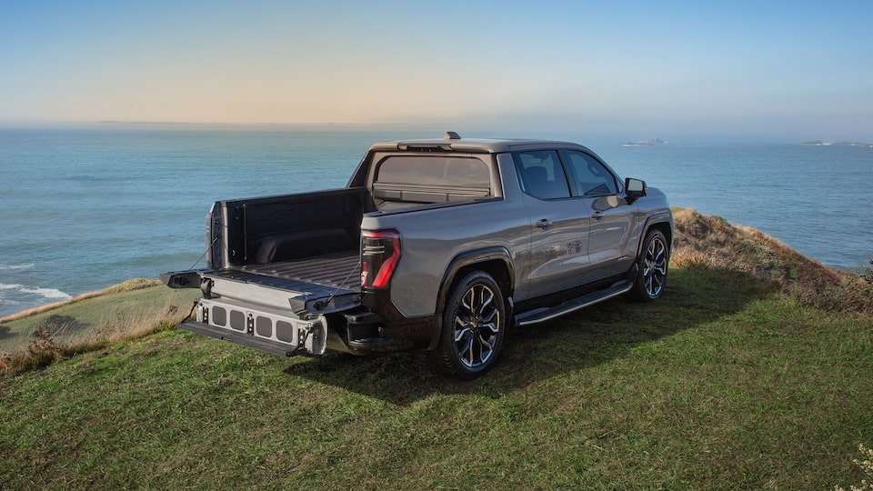 Rear Three-Quarter View of the Sierra EV Parked on a Hill Over Looking a Body of Water with the Truck's Tailgate Down