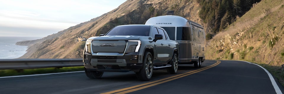 A 2025 GMC Sierra EV Pickup Truck Towing a Trailer with Mountains in the Background